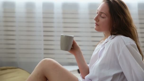 Woman in white mans shirt drinking coffee in bed — Stock Video