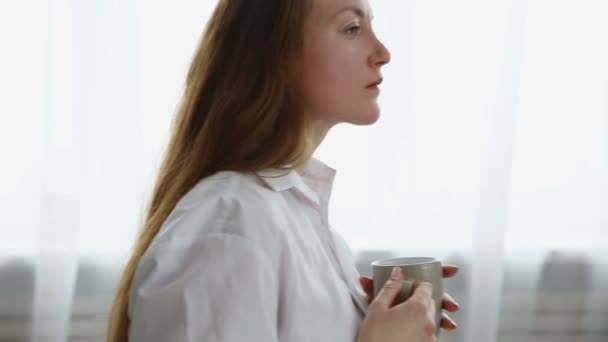 Vrouw in wit mans shirt drinken koffie thuis — Stockvideo