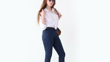 moda modern gençlik. şık kız kot pantolon, beyaz gömlek, deri sırt çantası ve gözlük ile beyaz duvara poz.
