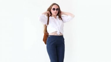 moda modern gençlik. şık kız kot pantolon, beyaz gömlek, deri sırt çantası ve gözlük ile beyaz duvara poz.