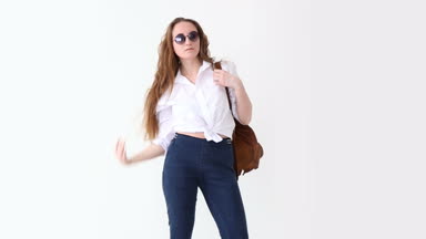 moda modern gençlik. şık kız kot pantolon, beyaz gömlek, deri sırt çantası ve gözlük ile beyaz duvara poz.