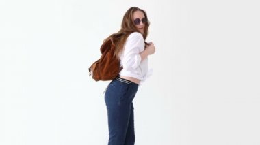 moda modern gençlik. şık kız kot pantolon, beyaz gömlek, deri sırt çantası ve gözlük ile beyaz duvara poz.