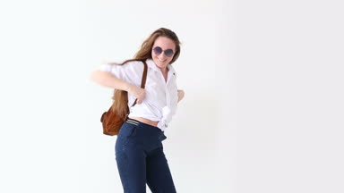 moda modern gençlik. şık kız kot pantolon, beyaz gömlek, deri sırt çantası ve gözlük ile beyaz duvara poz.
