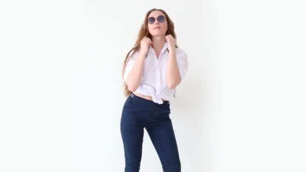 Мода современной молодежи. стильная девушка позирует против белой стены в джинсах, белой рубашке, с кожаным рюкзаком и очками . — стоковое видео