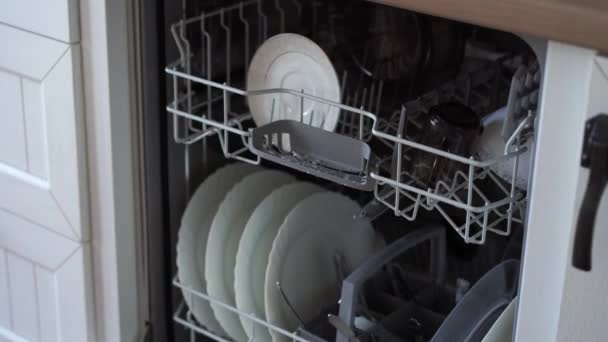 Жінка відкриває посудомийну машину і виймає чистий посуд — стокове відео