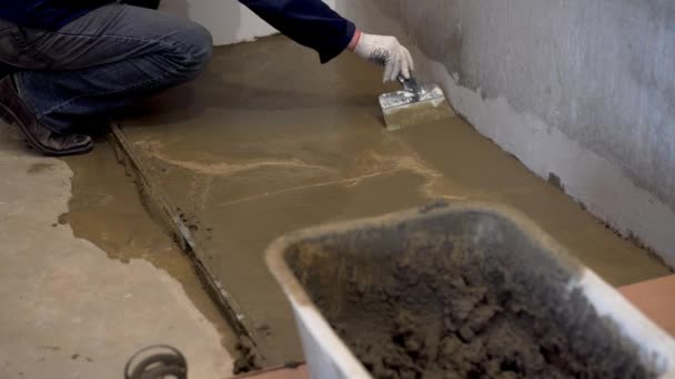 Reparatie van appartementen en huizen. de bouwer giet en egaliseert de betonnen vloer. — Stockvideo