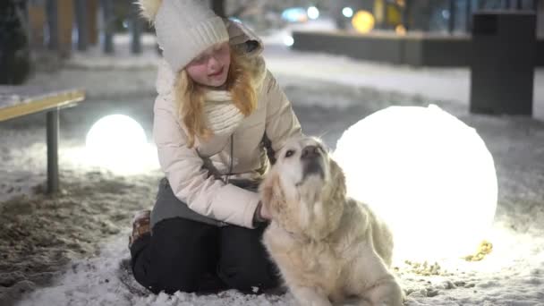 Счастливая жизнь домашних животных в семье. красивая девушка гладит свою собаку на улице зимой . — стоковое видео