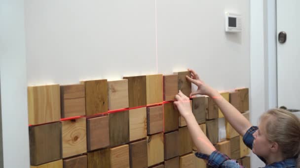 Originele moderne reparatie in een loft stijl. vrouw versiert een muur in een appartement met houten stukken — Stockvideo