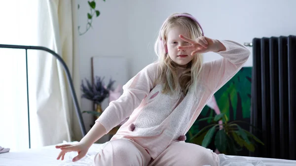 Modern élet generációs Z. tizenéves lány pizsamában és fejhallgató a szobában az ágyon zenét hallgat egy okostelefonról. — Stock Fotó