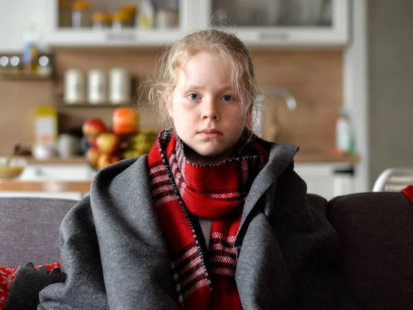 Chica caucásica fría en casa. retrato de un niño enfermo en una bufanda y a cuadros en el sofá en el apartamento — Foto de Stock