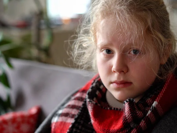 Koud Kaukasisch meisje thuis. portret van een ziek kind in een sjaal en geruit op de bank in het appartement — Stockfoto