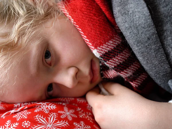 Chica caucásica fría en casa. retrato de un niño enfermo en una bufanda y a cuadros en el sofá en el apartamento —  Fotos de Stock