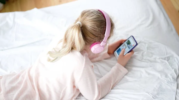 Modern life of generation Z. teenage girl in pajamas and headphones in the room on the bed listens to music from a smartphone. — 스톡 사진