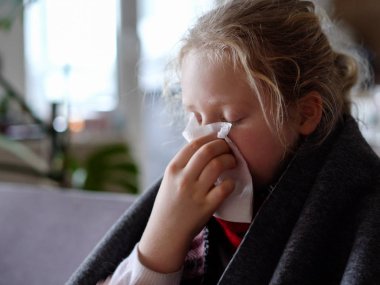 cold caucasian girl at home. portrait of a sick child in a scarf and plaid on the sofa in the apartment, the schoolgirl blows snot into a napkin