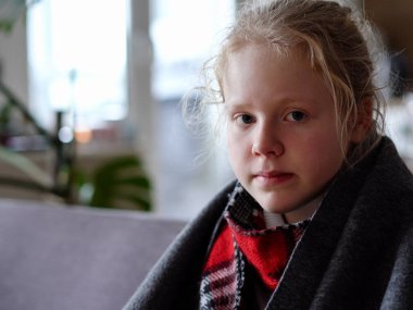 cold caucasian girl at home. portrait of a sick child in a scarf and plaid on the sofa in the apartment