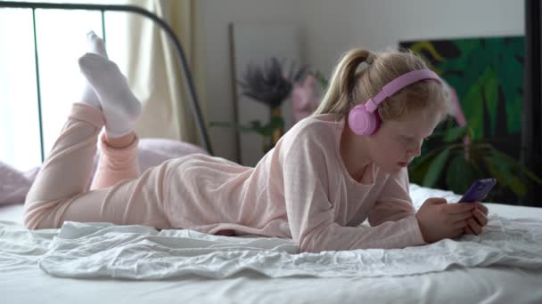 Vida moderna da geração Z. adolescente em pijama e fones de ouvido no quarto na cama escuta música de um smartphone . — Vídeo de Stock