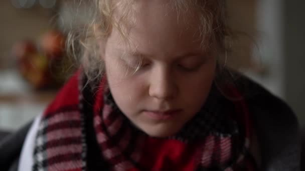 Portrét nemocného dítěte v šále a kostkovaném kostkovaném, dívka pojídající vývar na pohovce v bytě — Stock video