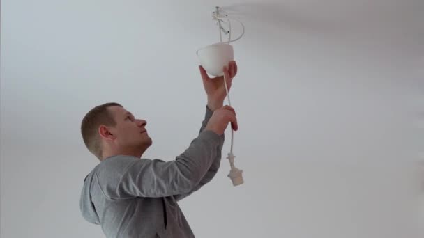 Reparatie en woninginrichting. een man hangt een lamp in de kamer aan het plafond. — Stockvideo