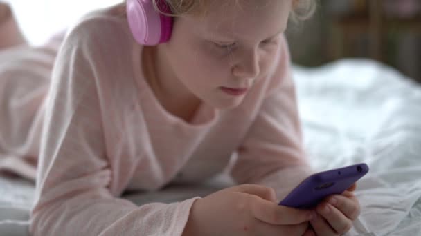 Moderní život generace Z. dospívající dívka v pyžamu a sluchátka v místnosti na posteli poslouchá hudbu z chytrého telefonu. — Stock video