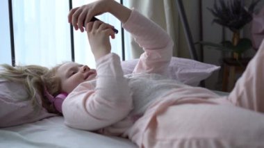 modern life of generation Z. teenage girl in pajamas and headphones in the room on the bed listens to music from a smartphone.