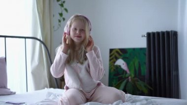 modern life of generation Z. teenage girl in pajamas and headphones in the room on the bed listens to music from a smartphone.