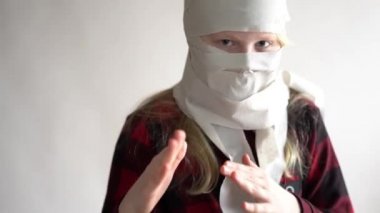 Komik bir video. Koronavirüs salgını yüzünden karantinaya alınmış. Gri arka planda poz veren tuvalet kağıdındaki maskeli kız..