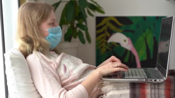 コロナウイルス感染症の隔離。感染した覆面の女性はラップトップで自宅で働いています. — ストック動画