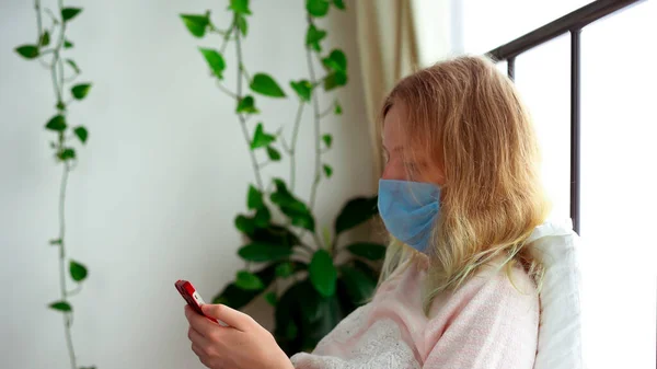 Cuarentena por epidemia de coronavirus. Una mujer infectada con una máscara está chateando a través de un enlace de vídeo en un teléfono inteligente . —  Fotos de Stock
