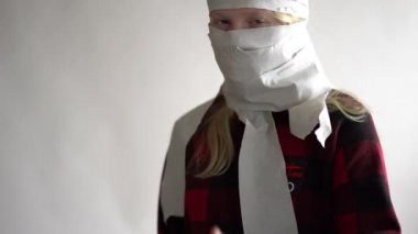 Komik bir video. Koronavirüs salgını yüzünden karantinaya alınmış. Gri arka planda poz veren tuvalet kağıdındaki maskeli kız..