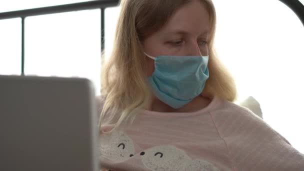 Karantén a koronavírus járvány miatt. Egy fertőzött maszkos nő dolgozik otthon egy laptoppal.. — Stock videók