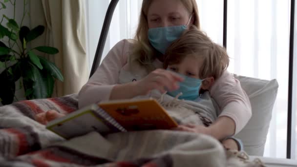 Quarantäne für Coronavirus-Epidemie. Maskierte Mutter und kleiner Sohn liegen im Bett im Schlafzimmer. — Stockvideo