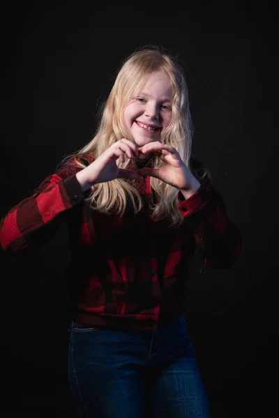 Happy schoolgirl posing in studio on a black background - shows hands signs hearts — Stock Photo, Image