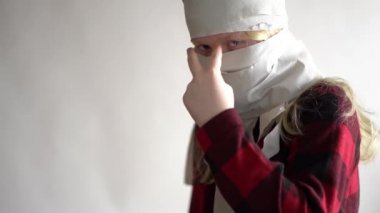 Komik bir video. Koronavirüs salgını yüzünden karantinaya alınmış. Gri arka planda poz veren tuvalet kağıdındaki maskeli kız..