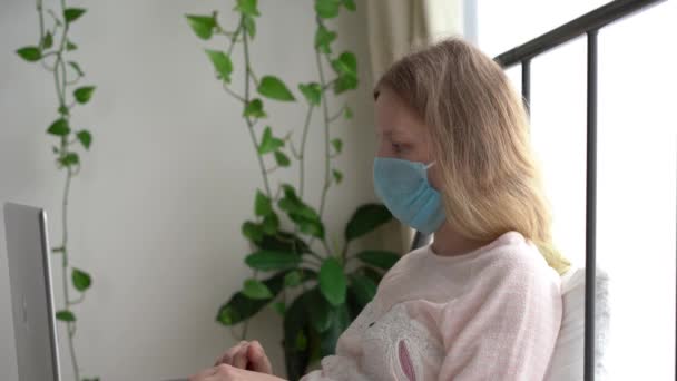 Quarantaine voor coronavirusepidemie. Een geïnfecteerde gemaskerde vrouw werkt thuis met een laptop. — Stockvideo