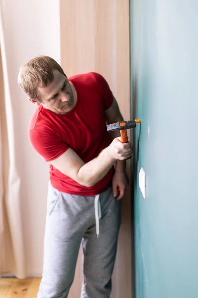 Reparação e decoração. um homem dirige uma tomada de parede com um martelo — Fotografia de Stock