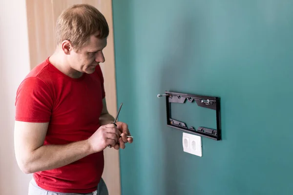 Reparação e decoração. marido por uma hora de serviço. um homem anexa um suporte de TV a uma parede . — Fotografia de Stock