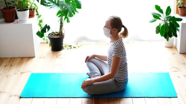 Stanna hemma. maskerad kvinna som gör yoga i vardagsrummet under karantänen — Stockvideo