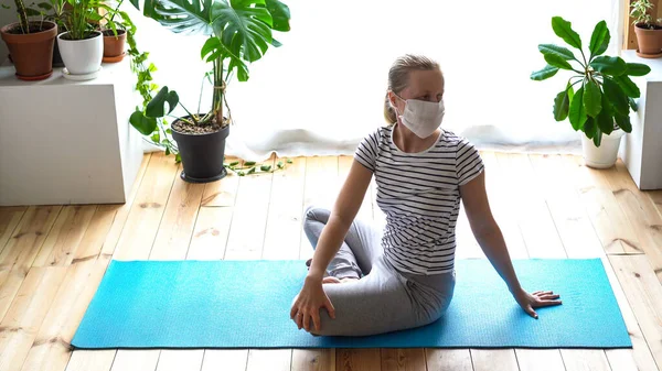 Stanna hemma. maskerad kvinna som gör yoga i vardagsrummet under karantänen — Stockfoto