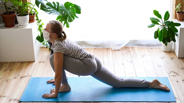 Stanna hemma. maskerad kvinna som gör yoga i vardagsrummet under karantänen — Stockfoto