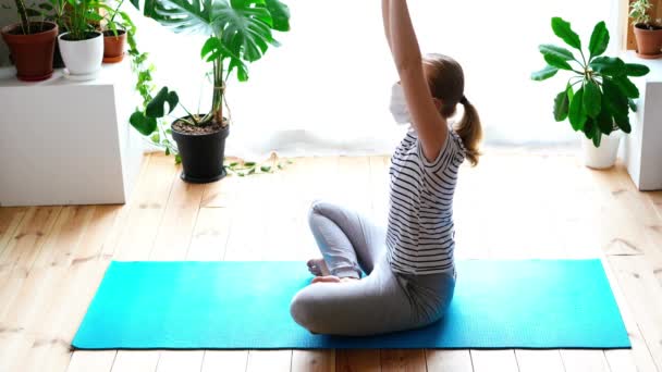 Stanna hemma. maskerad kvinna som gör yoga i vardagsrummet under karantänen — Stockvideo