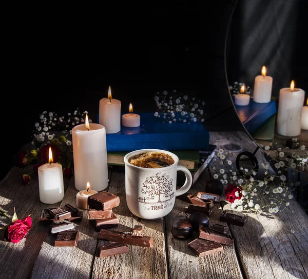 Brinnande ljus, en kopp kaffe och choklad på ett träbord. Reflektion i spegeln. — Stockfoto
