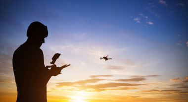 Drone pilot with quadrocopter. Silhouette against the sunset sky clipart