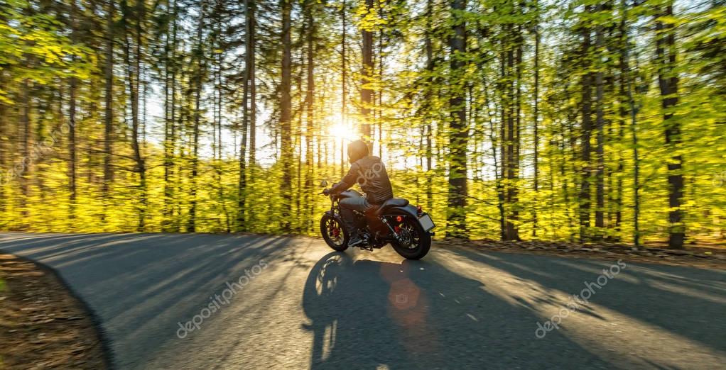 Motorcycle driver driving in forest, beautiful sunset