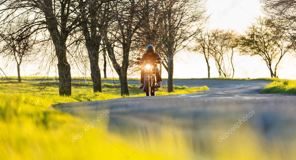 Motorcycle driver driving in sunset, blur grass on foreground