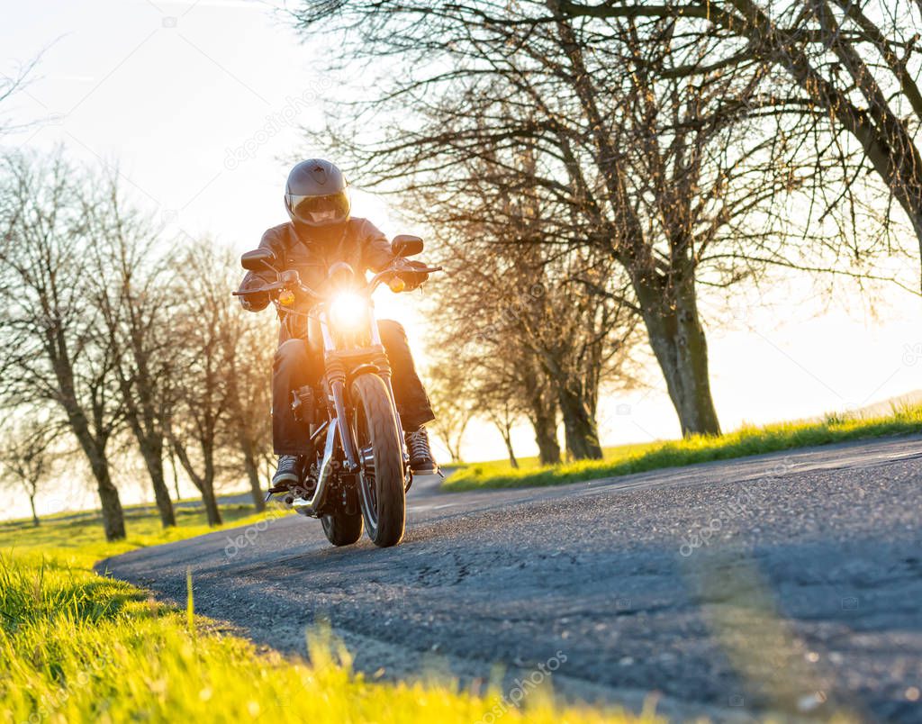 Motorcycle driver driving in sunset, blur grass on foreground