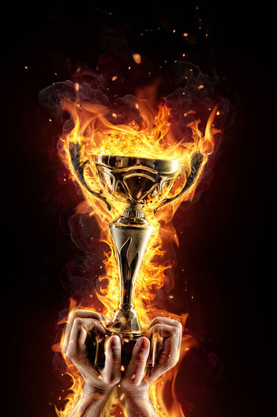 Man hands holding burning gold trophy cup as a winner