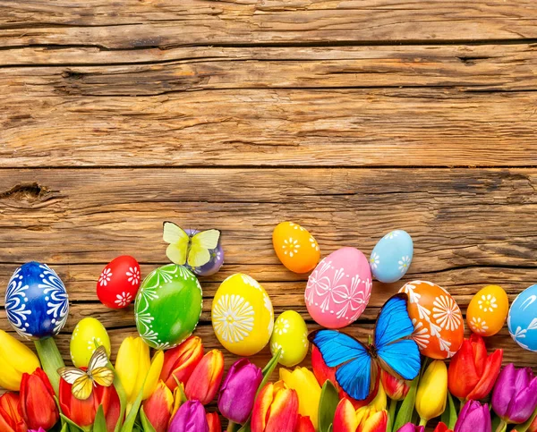 Ovos de Páscoa com tulipas e borboleta em tábua de madeira — Fotografia de Stock