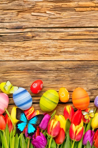 Huevos de Pascua con tulipanes y mariposa sobre tabla de madera —  Fotos de Stock