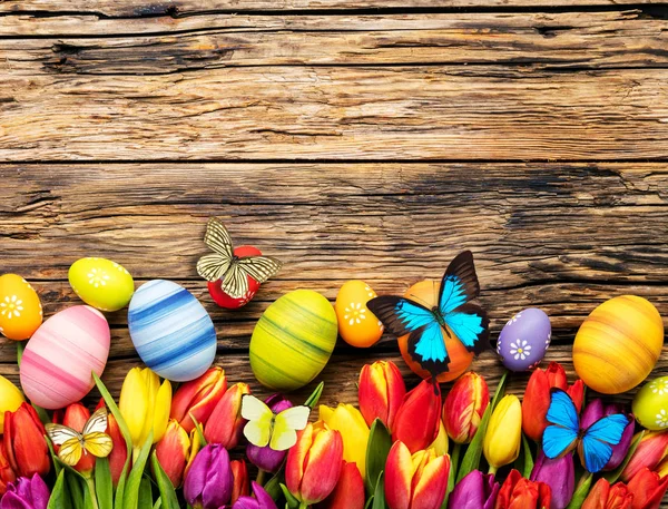 Uova di Pasqua con tulipani e farfalla su tavola di legno — Foto Stock