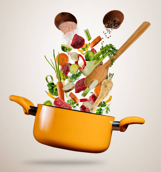 Fresh vegetable and meat flying into a pot on gray background